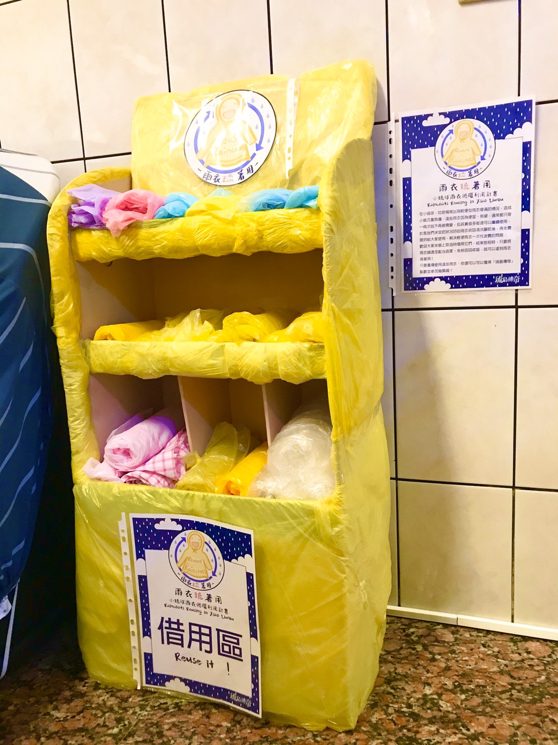 The “Reusable Raincoats in Liuqiu” racks are adapted from idled racks for displaying goods at convenience stores. Since these are paper racks, the organizer wrapped them up with a disposable raincoat, so that they won’t be damaged on rainy days.  (Photo credit: Chen Hung-chun)